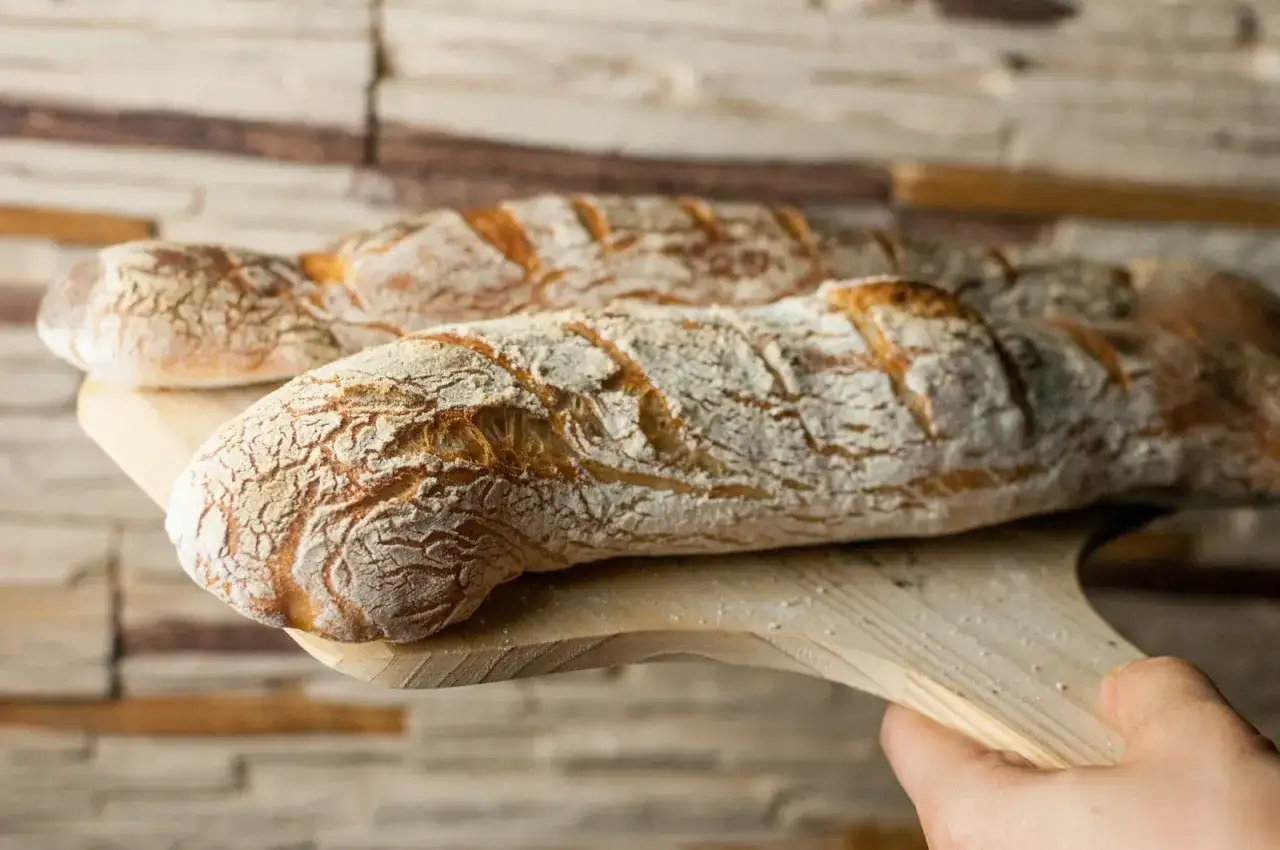 Dwie świeże, chrupiące bagietki francuskie na drewnianej desce, gotowe do podania.