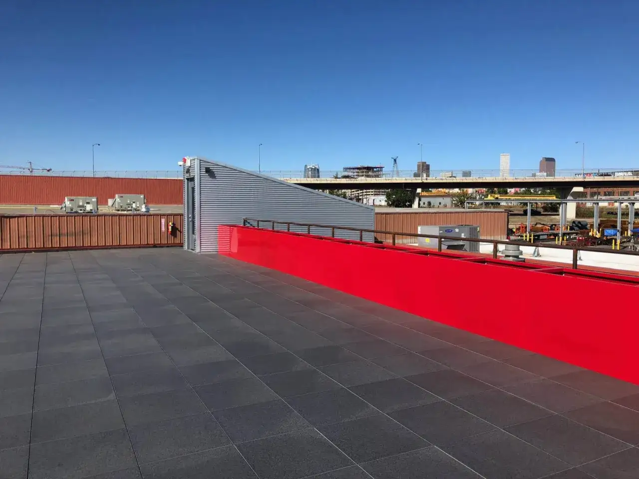 Moderne Dachterrasse mit grauem Fliesenboden und leuchtend roter Br&uuml;stung. Ein idealer Ort, um den Blick auf die Stadt zu genie&szlig;en.