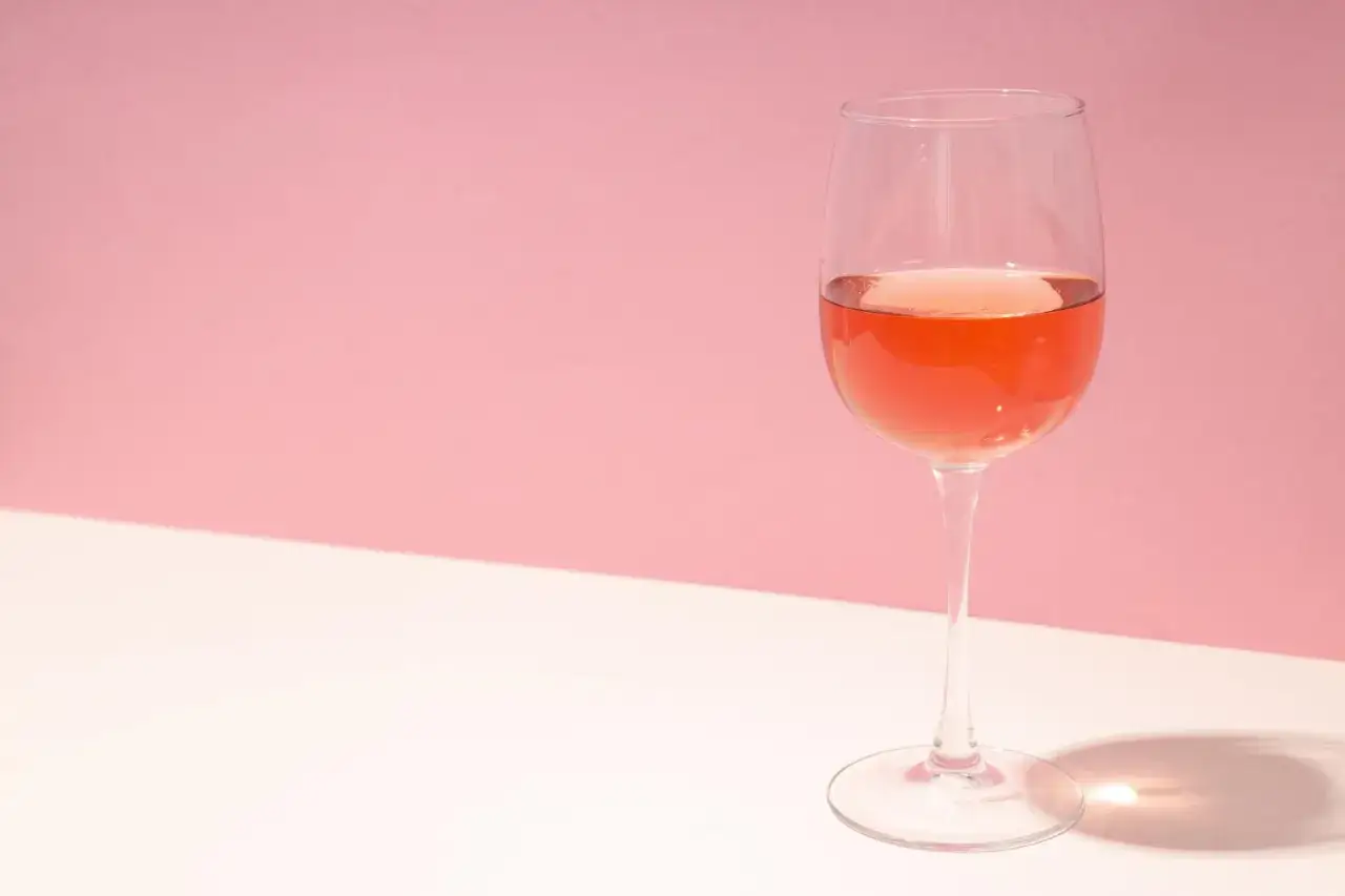 Un verre de vin ros&eacute; tr&egrave;s clair sur un fond rose et blanc, avec une ombre projet&eacute;e.