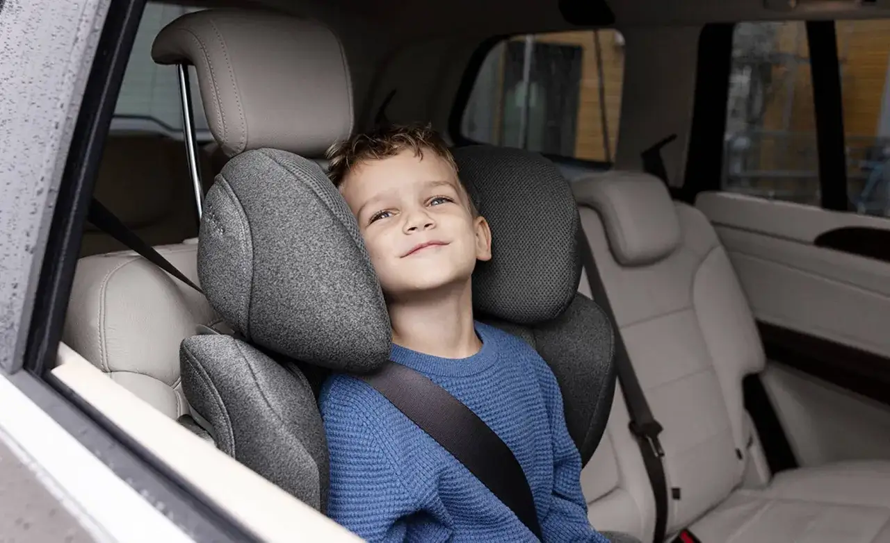 Niño sonriente en un alzador o silla coche, con cinturón de seguridad puesto, listo para el viaje.
