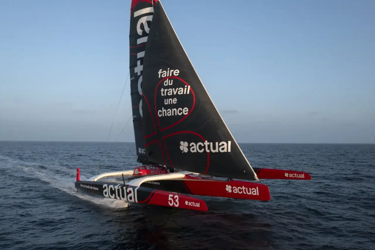 Trimaran Actual, sponsorisé par SVR Lazartigue, navigue sur une mer bleue. La voile porte le message