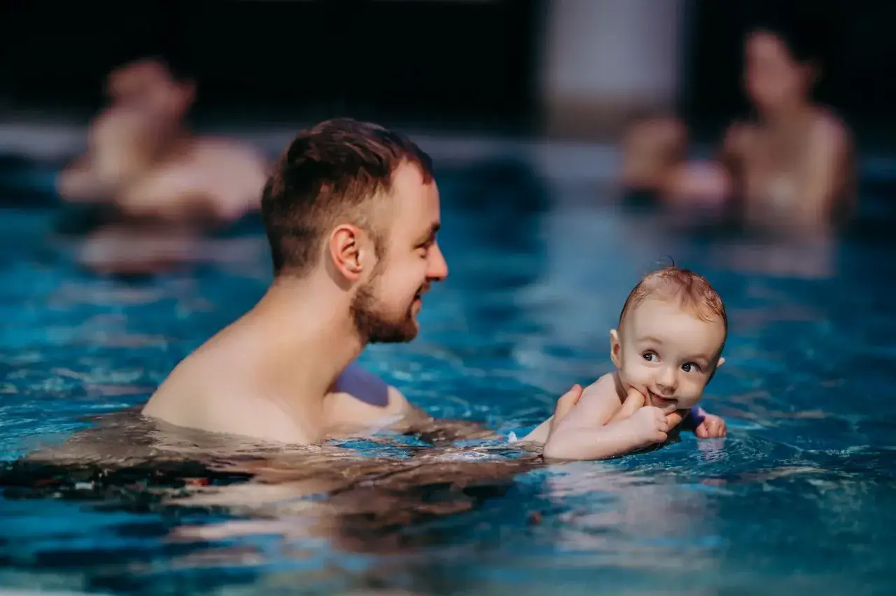 Uśmiechnięty ojciec i dziecko w wodzie. Radosne chwile w akademii pływania Fala.