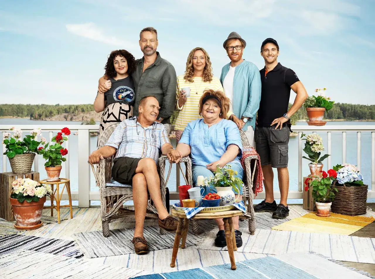 En familj samlad på en altan vid vattnet. De verkar njuta av varandras sällskap under udda veckor, kanske under semestern.