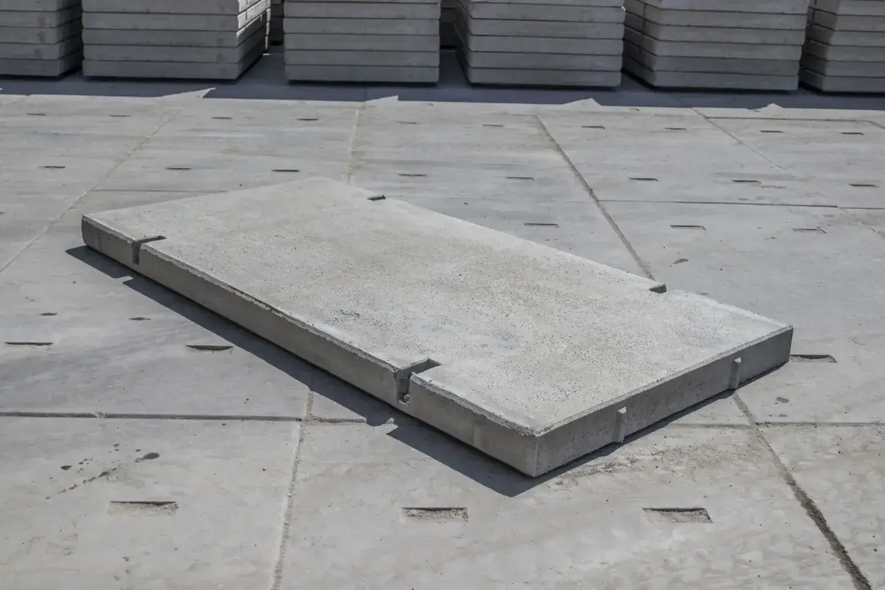 Pojedyncza płyta drogowa betonowa leży na placu budowy, obok ułożonych w stosy płyt.
