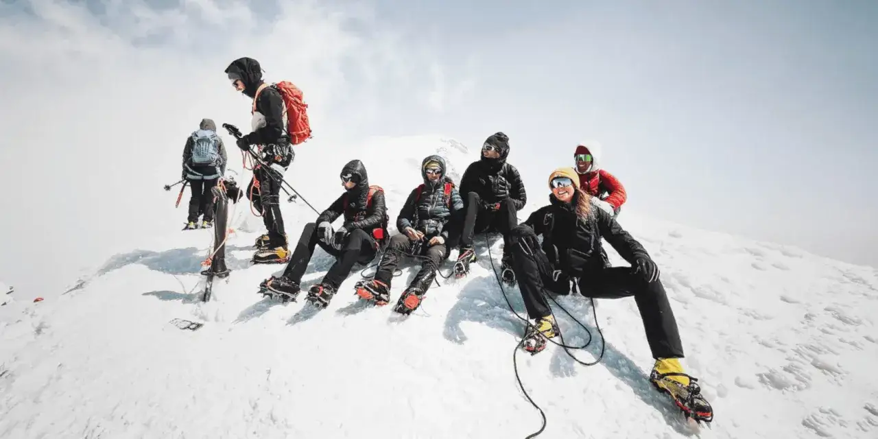 Une équipe de grimpeurs, dont Balin Miller, se repose sur une crête enneigée, équipés de crampons et de piolets, prêts pour l'ascension.