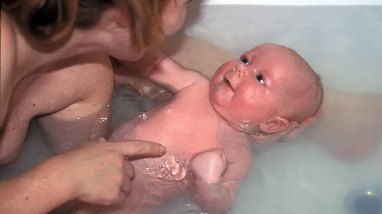 Ein Baby genießt sein Bad, während eine Hand sanft über seine Haut streicht.