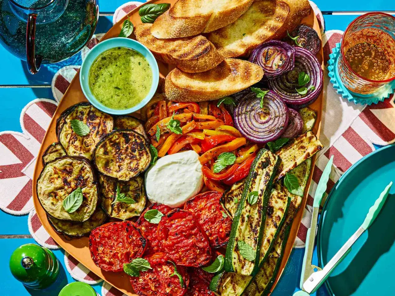 Kolorowa deska pełna grillowanych warzyw: cukinii, bakłażana, papryki, cebuli i pomidorów. Idealne warzywa na grilla z sosem i pieczywem.