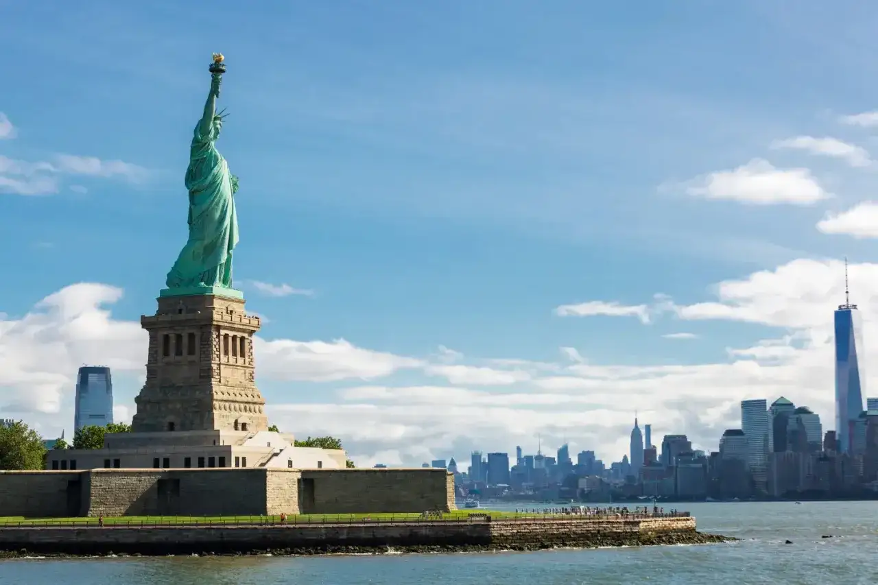 Statua Wolności wita przybyszów w USA. W tle panorama Nowego Jorku z wieżowcami.