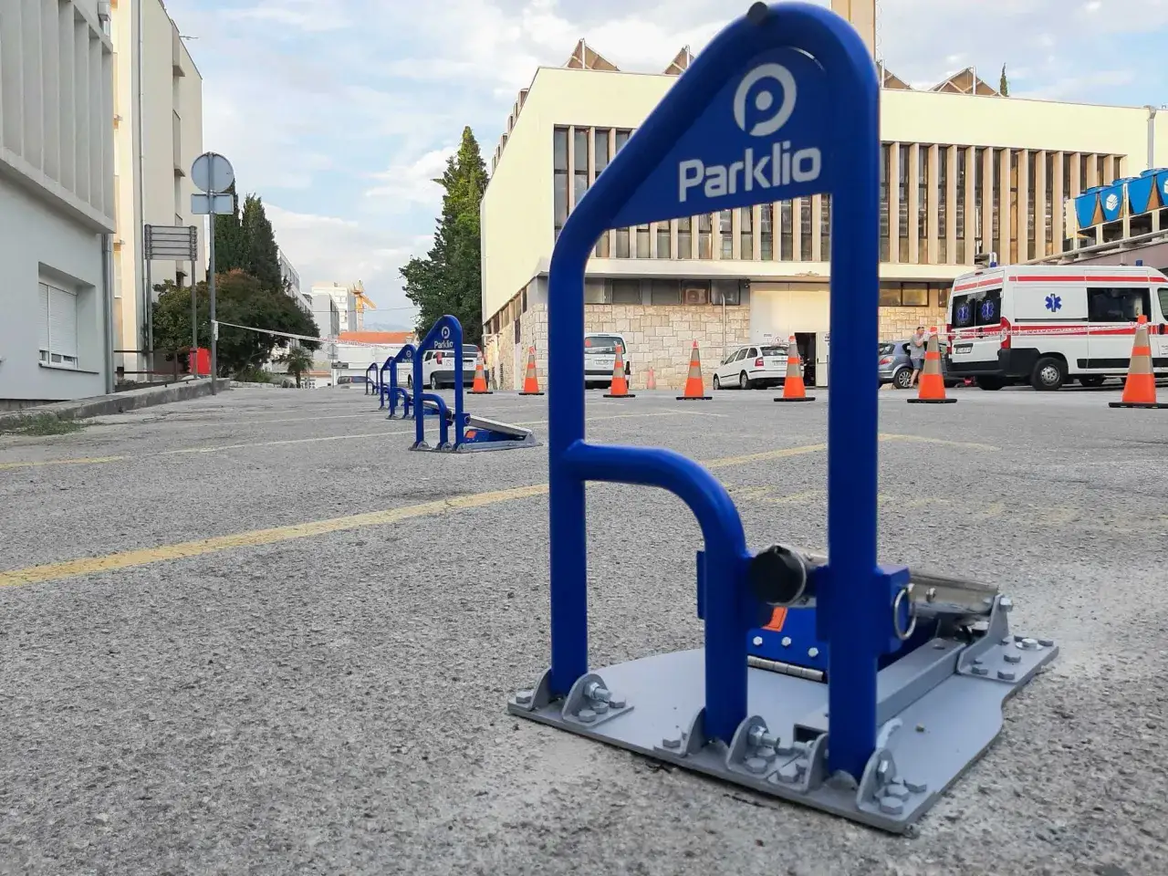 Niebieska blokada wjazdu na posesję z logo Parklio, ustawiona na parkingu przed budynkiem.