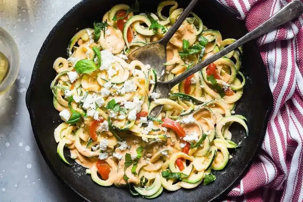 Pyszny makaron keto z cukinii w kremowym sosie, posypany fetą i bazylią, podany w żeliwnej patelni.