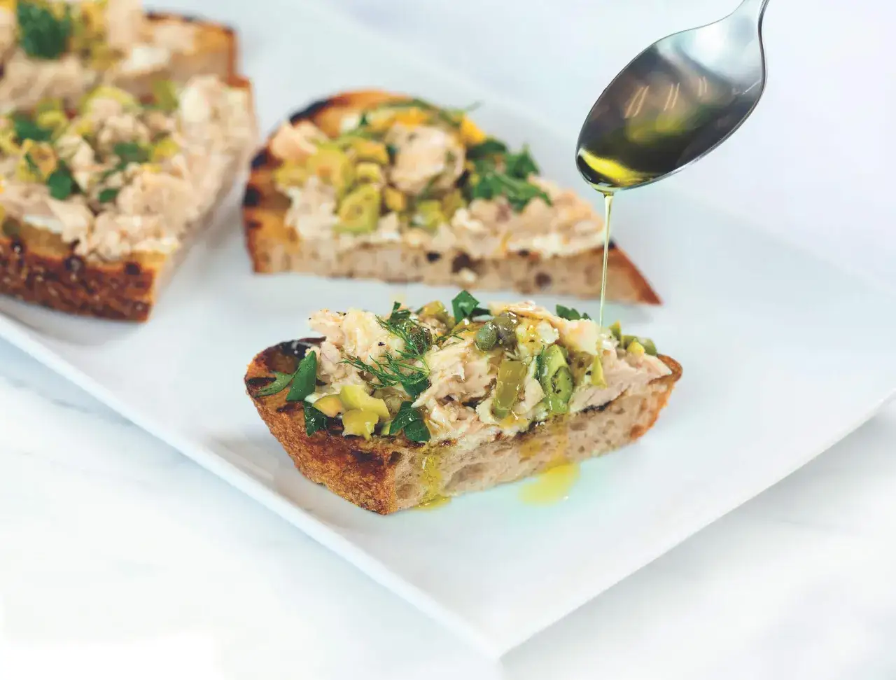 Tartines de p&acirc;t&eacute; de thon rapide, garnies d'olives et d'herbes, arros&eacute;es d'huile d'olive.
