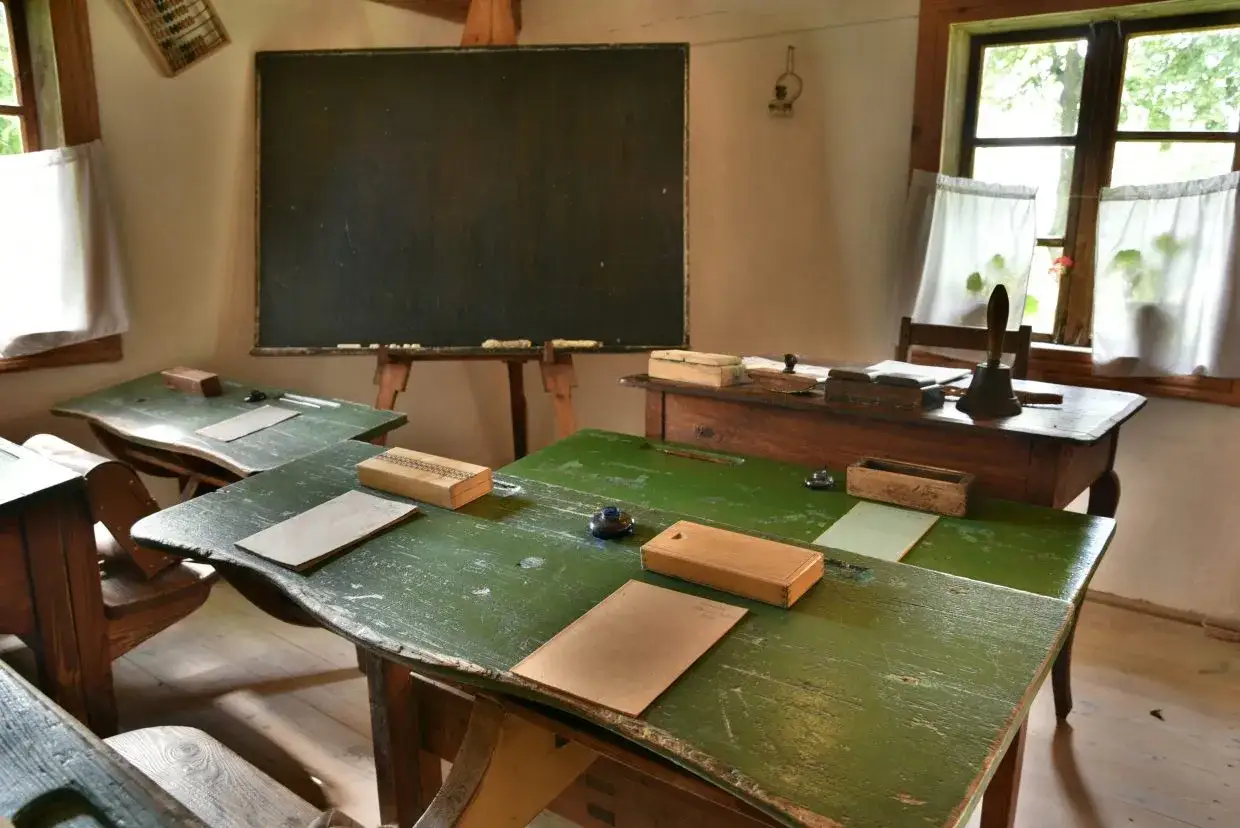 Klasa szkolna z ławkami, tablicą i dzwonkiem, przypominająca pruski system edukacji.