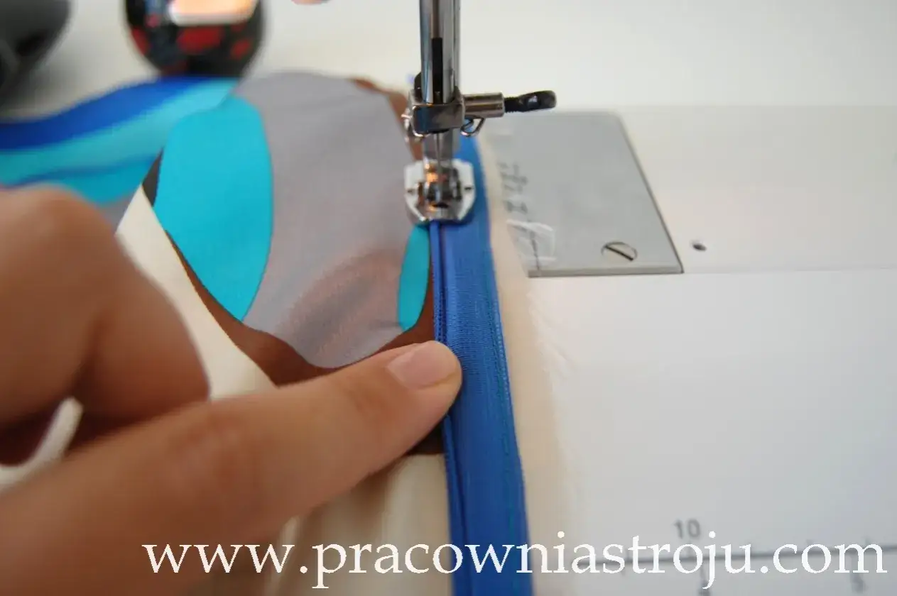 Ręka przytrzymuje materiał, a maszyną do szycia wszywany jest zamek kryty. Tutorial: jak wszyć zamek kryty.