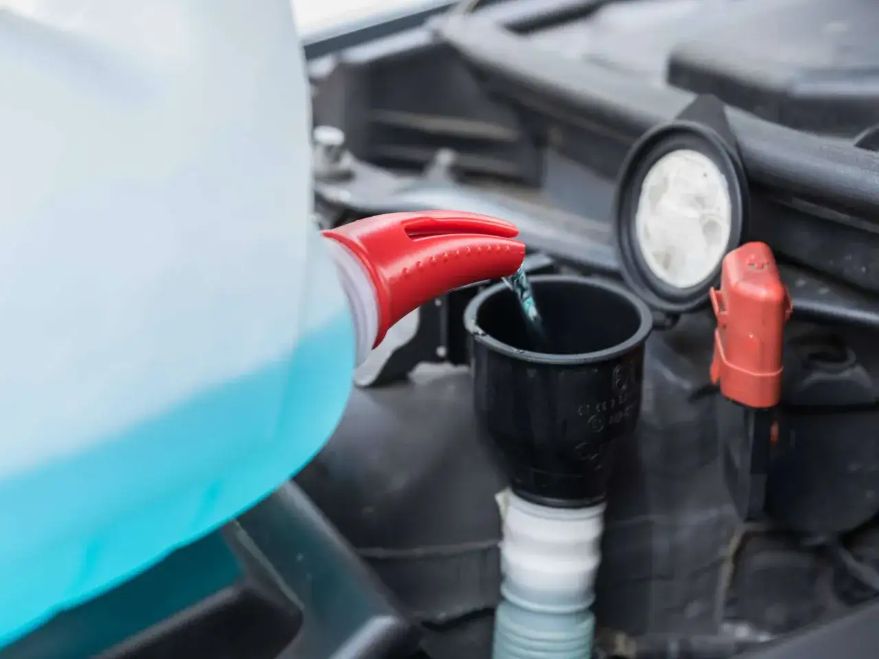 Blaues Scheibenwischwasser wird aus einem Behälter mit rotem Ausguss in einen schwarzen Trichter gegossen, um es aufzufüllen.