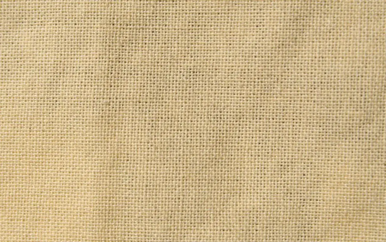 Gros plan sur la texture d'une matière toile de lin beige, avec ses fils entrelacés formant un motif régulier.