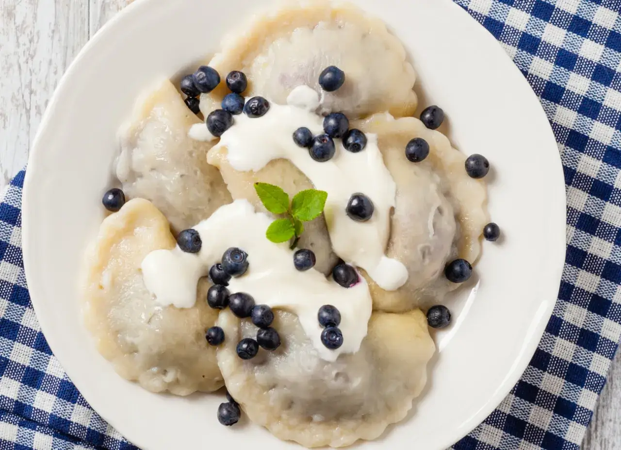 Pyszne pierogi z jagodami, polane śmietaną i posypane świeżymi owocami. Letnia uczta na talerzu.