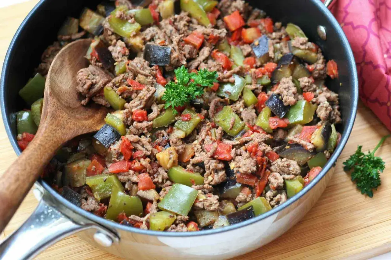 Herzhaftes Hackfleischgericht mit Auberginen und Paprika, perfekt für Low Carb. Ein Holzlöffel liegt bereit.