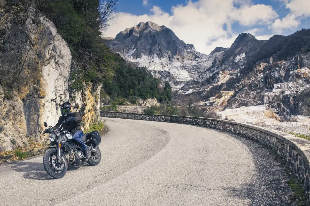 Motociclista su strada tortuosa, ideale per itinerari moto Toscana 1 giorno, con cave di marmo sullo sfondo.
