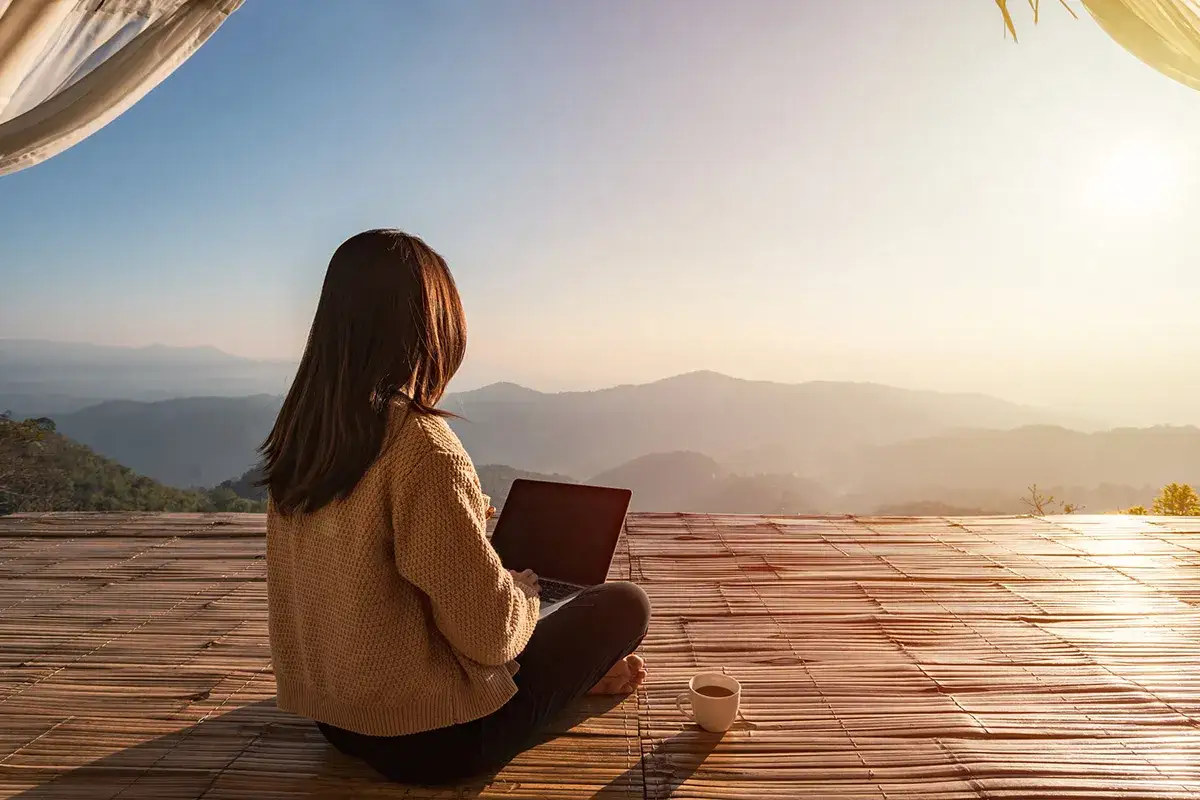 Frau arbeitet am Laptop mit Blick auf Berge. Perfekte Workation in Europa.