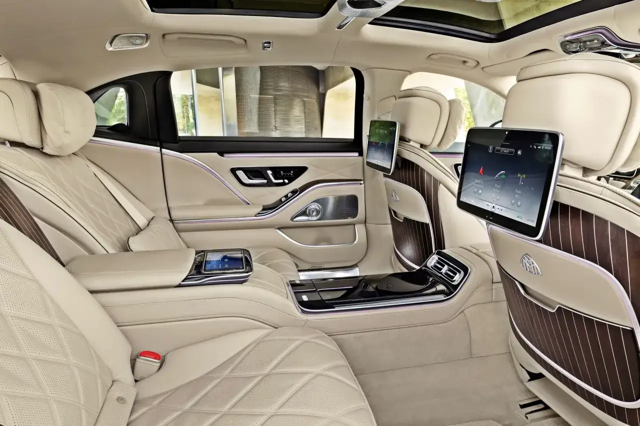 Luksusowe wnętrze Maybach S580 z kremową skórzaną tapicerką, ekranami dla pasażerów i ambientowym oświetleniem.
