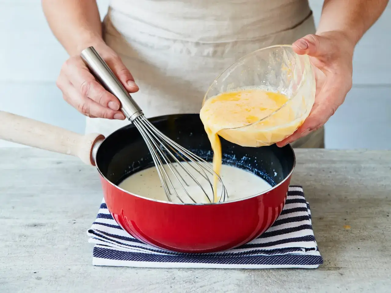 Schlagen Sie Eier in Milch ein, um Vanillepudding selber zu machen. Ein Schneebesen hilft beim Vermischen.