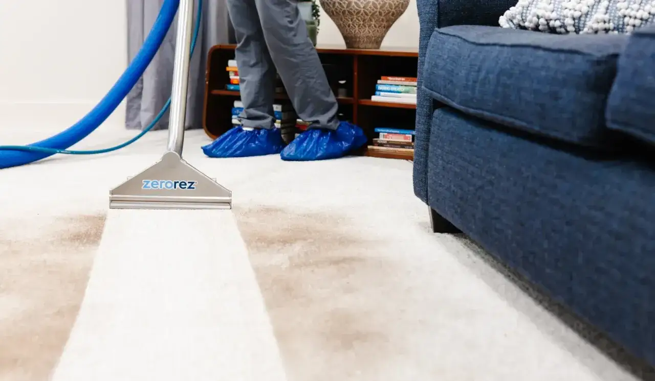 A professional demonstrates how to clean a carpet with a Zerorez machine, leaving a clean strip on the beige rug.