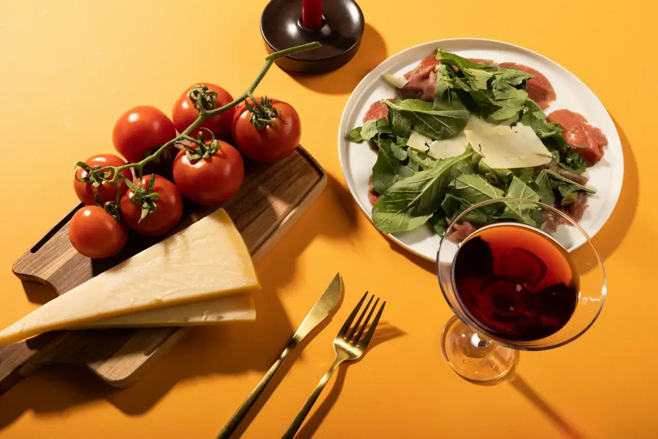 Grana Padano i parmezan na desce, pomidory, carpaccio z rukolą i kieliszek czerwonego wina.