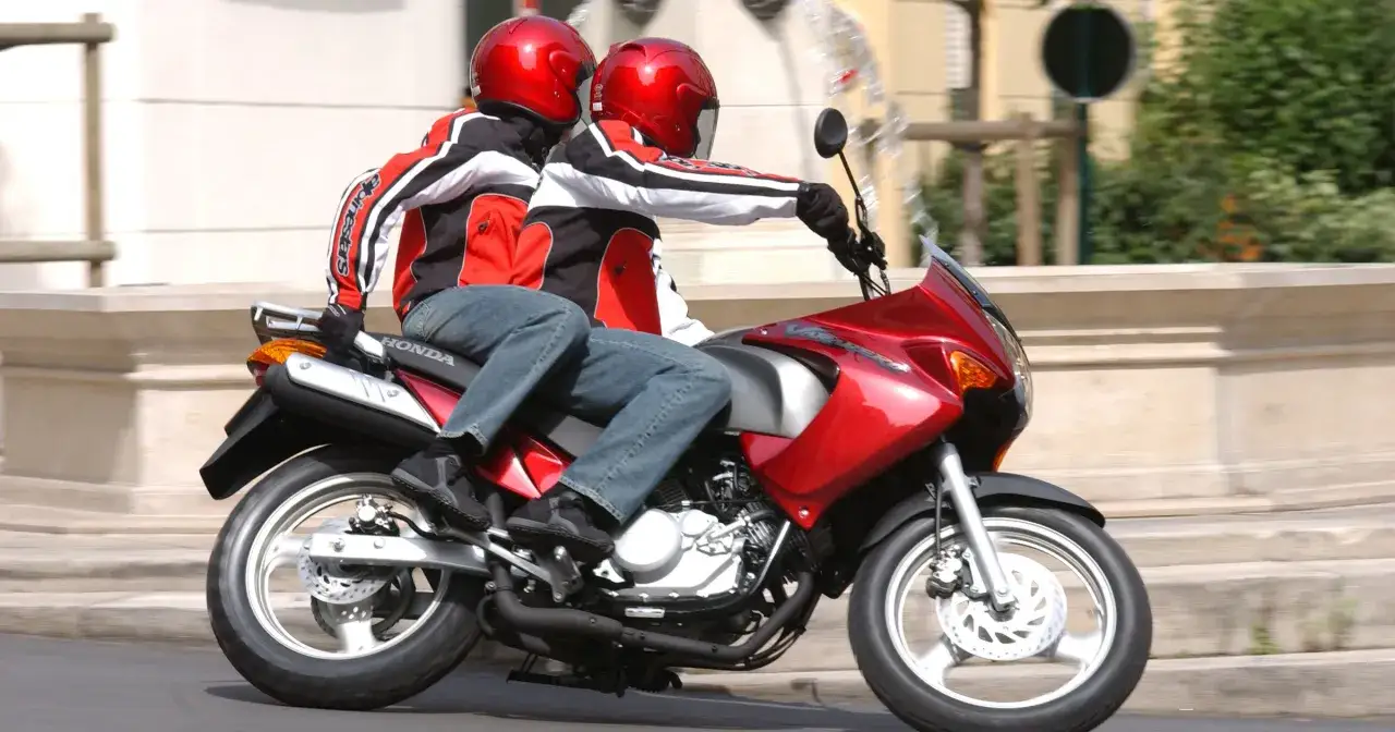 Dwie osoby w kaskach i kurtkach jadą na czerwonym motocyklu. Kierowca i pasażer, kat a1, cieszą się jazdą.