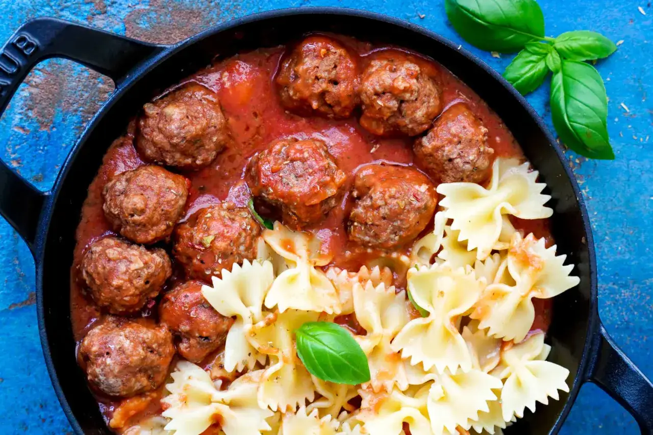 Herzhafte Fleischbällchen in Tomatensauce mit Farfalle-Nudeln, ein köstliches polpette rezept. Frischer Basilikum garniert das Gericht.