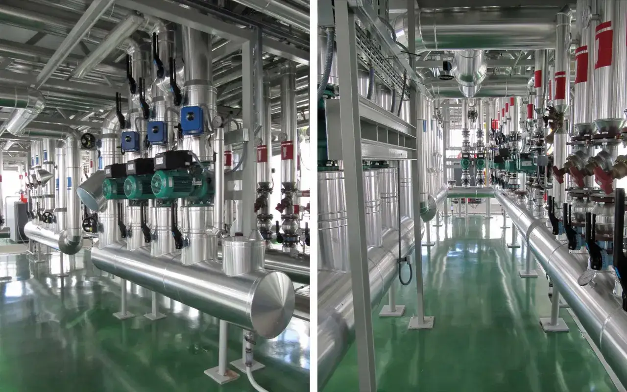 Instalación industrial con tuberías de hierro y aluminio, bombas verdes y válvulas rojas.