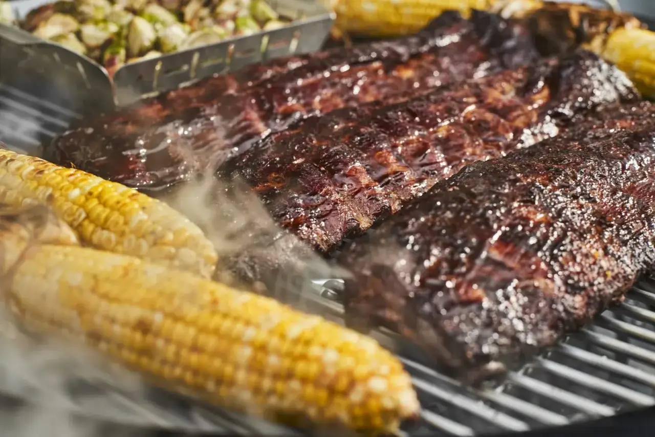 Żeberka i kukurydza na grillu, parujące i lśniące. To właśnie **bbq co to znaczy** &ndash; pyszne jedzenie z ognia!