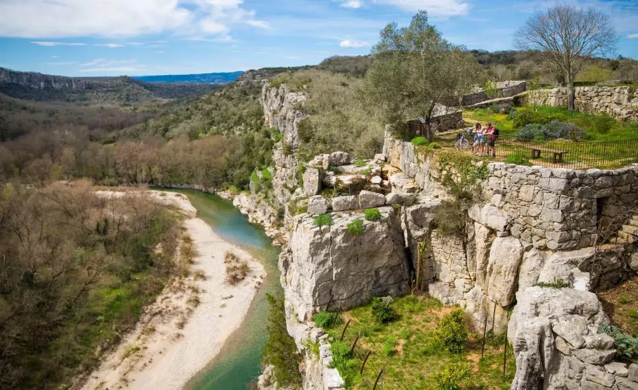 Vue panoramique sur la rivière et les falaises de la gr ardeche. Deux cyclistes admirent le paysage depuis un promontoire rocheux.