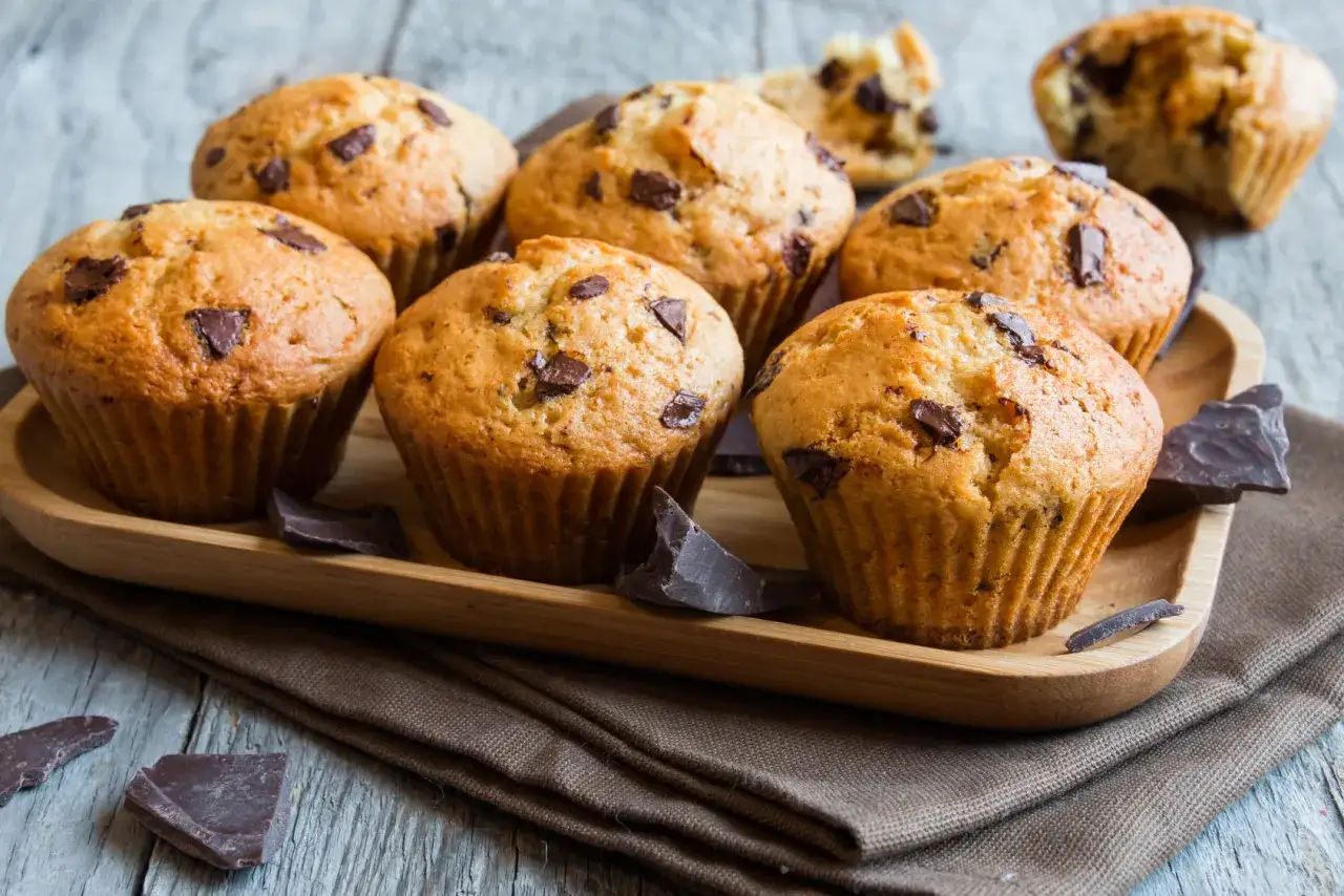 Puszyste muffinki waniliowe z czekoladą, ułożone na drewnianej tacy, obok kawałków gorzkiej czekolady.