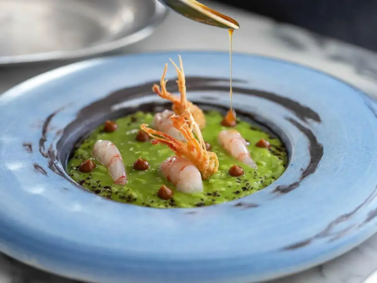 Gamberi e crema di piselli in un piatto da ristorante 1 stella Michelin. Un filo d'olio dorato completa l'opera.
