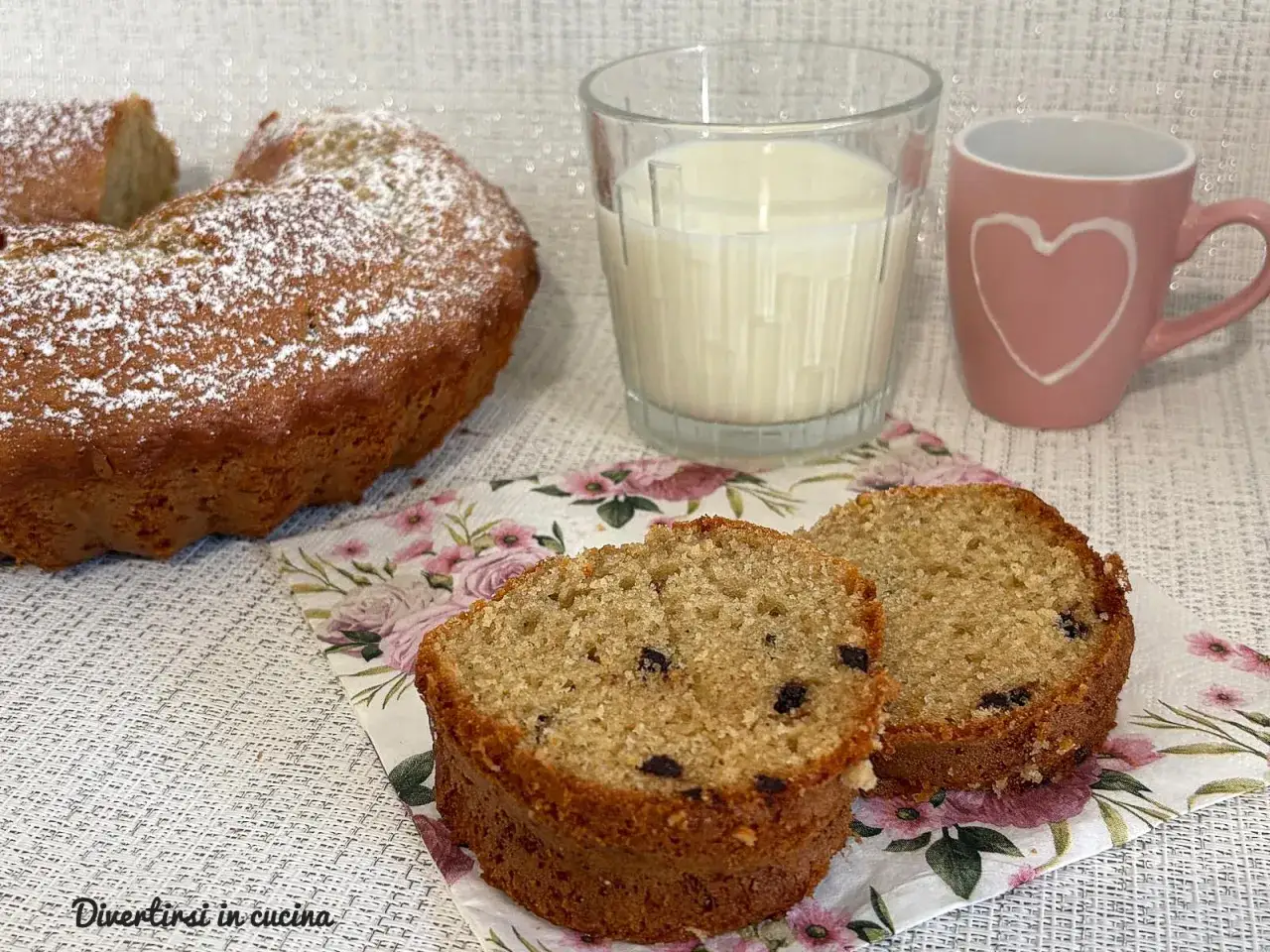 Bizcocho casero con chispas de chocolate, perfecto para tus recetas para merendar. Acompa&ntilde;ado de un vaso de leche y una taza rosa con un coraz&oacute;n.