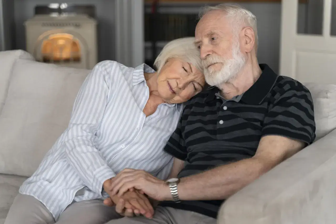 Un couple âgé se repose sur un canapé, la femme s'appuyant sur l'épaule de son mari. Une scène touchante qui évoque le besoin d'aide pour EHPAD Alzheimer.