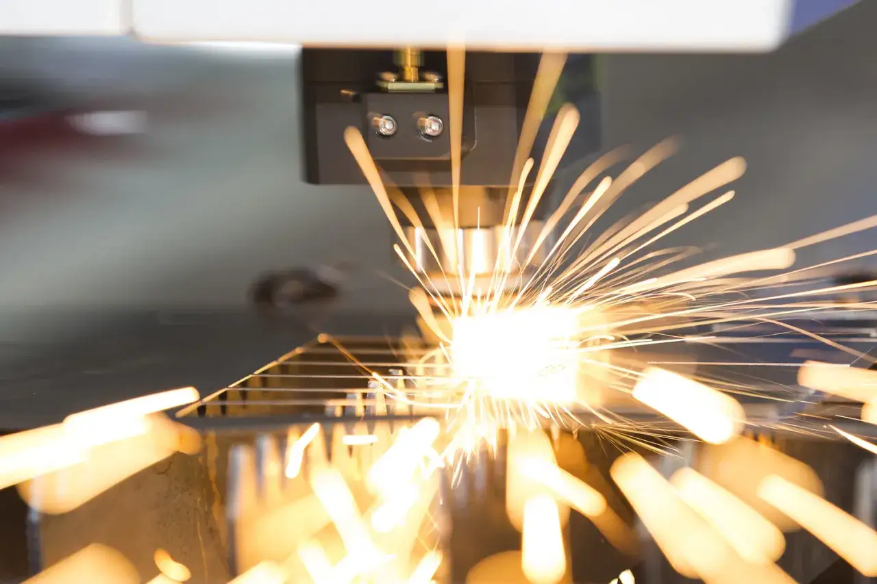 Precyzyjne cięcie metalu przez laser, tworzące snopy iskier. To przykład, co to jest ablacja laserowa w praktyce przemysłowej.