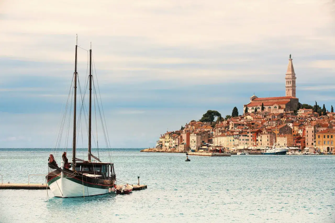 Un veliero ormeggiato nel mare Adriatico, con la pittoresca citt&agrave; di Rovigno sullo sfondo. Un esempio perfetto di cosa vedere in Croazia.