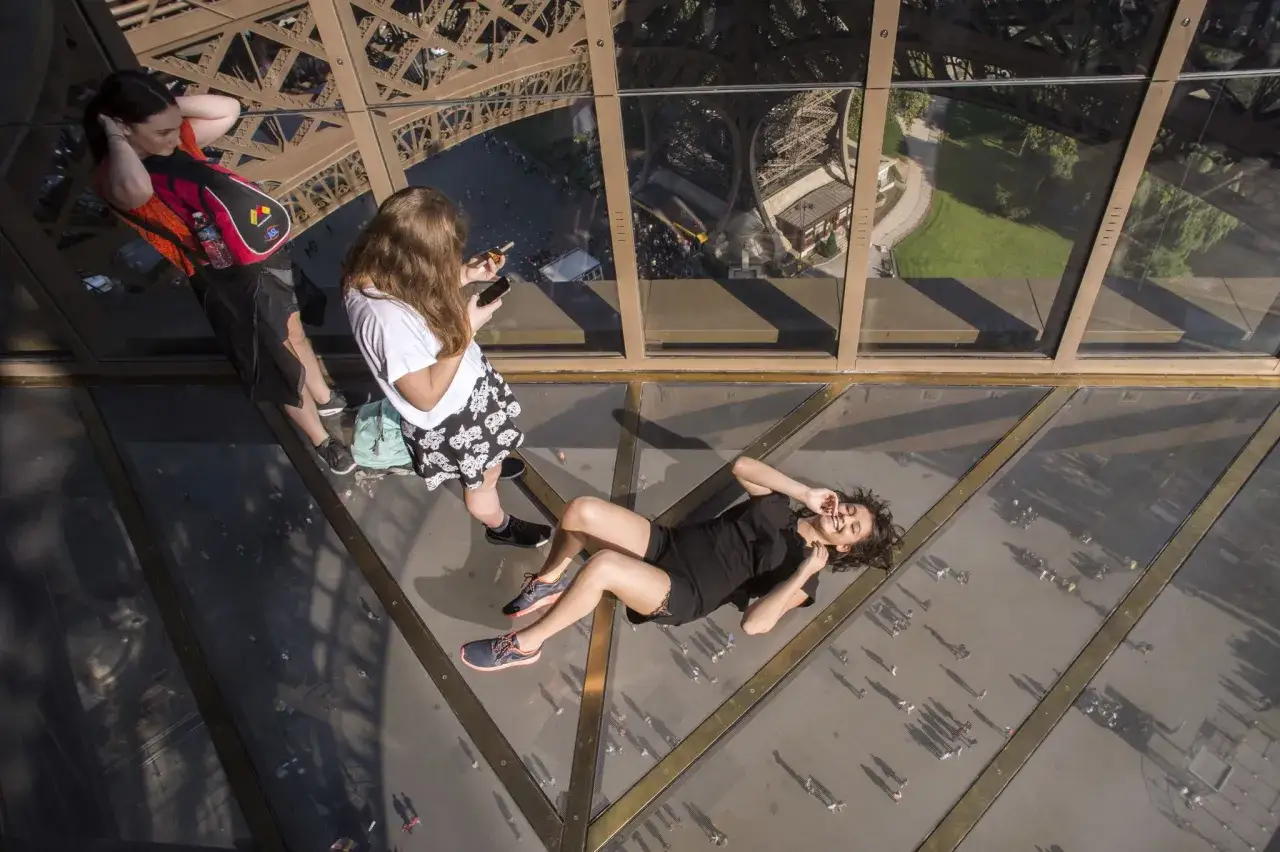 Des jeunes profitent de la vue vertigineuse en se couchant sur le sol en verre de la Tour Eiffel.