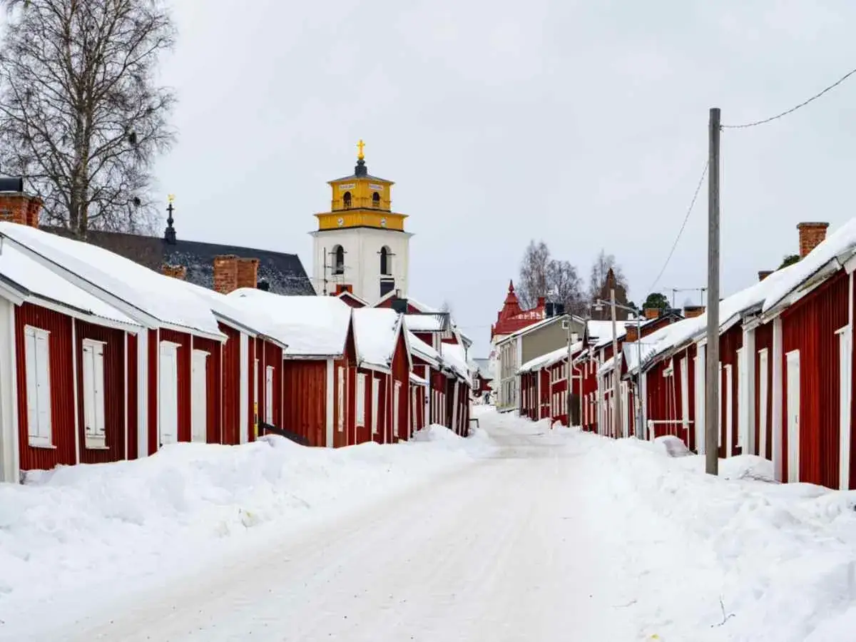 Snöig gata i Luleå med röda trähus och en kyrka i bakgrunden. Perfekt för luleå travel.