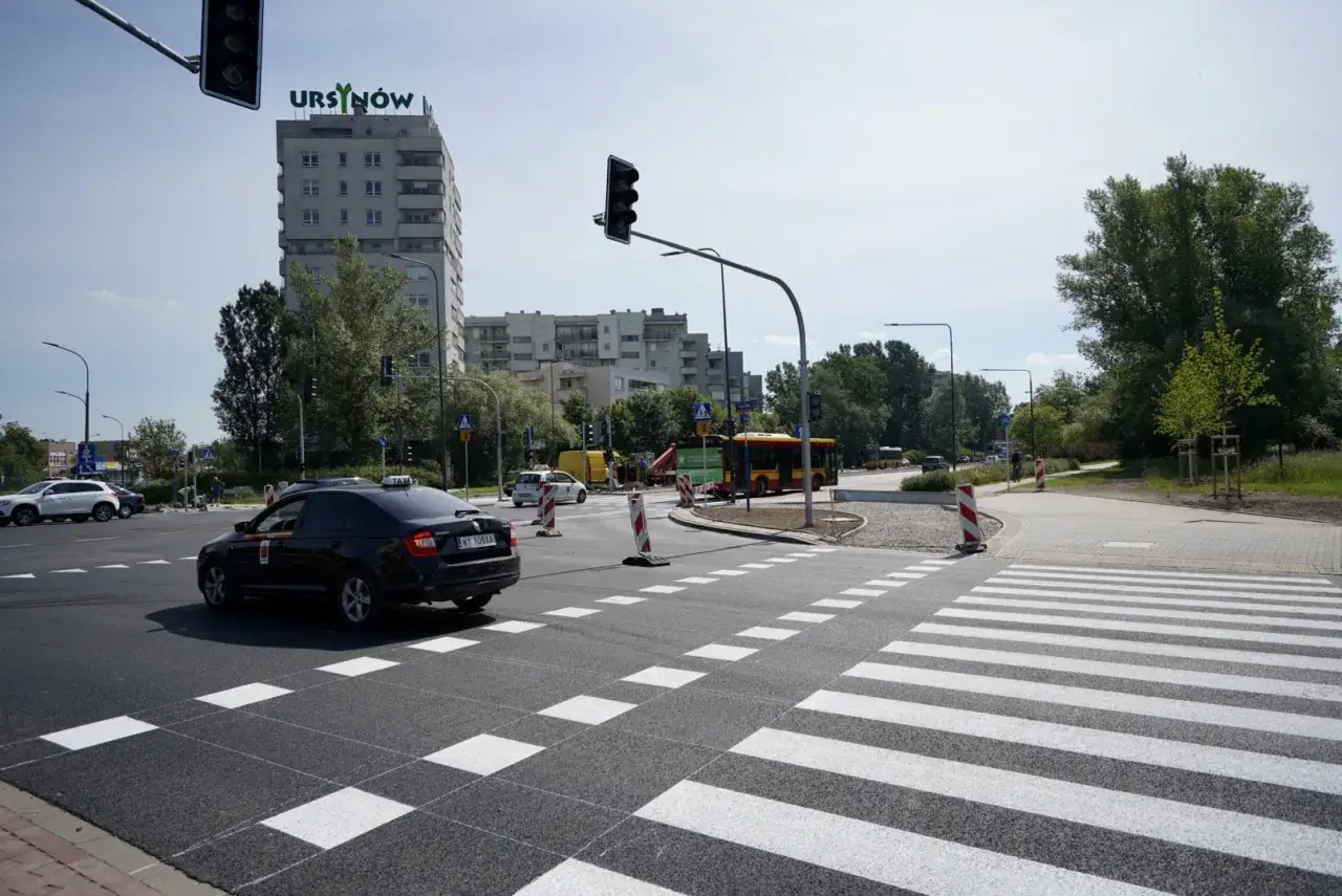 Skrzyżowanie z nowym pasem ruchu i sygnalizacją świetlną. Czarna taksówka czeka na zielone światło.