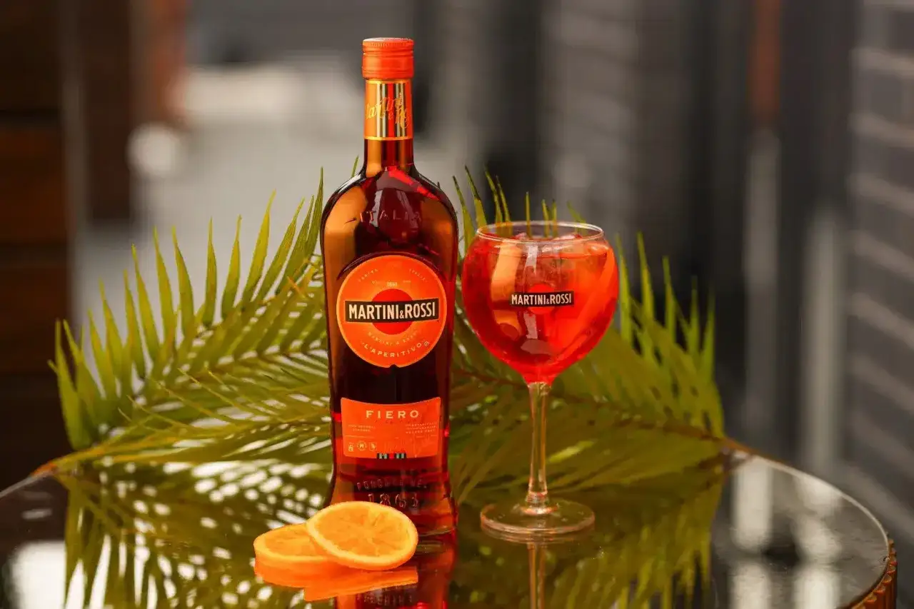 Orzeźwiający drink z Martini Fiero i Aperol, podany w kieliszku z lodem i plasterkami pomarańczy, obok butelki Martini Fiero.