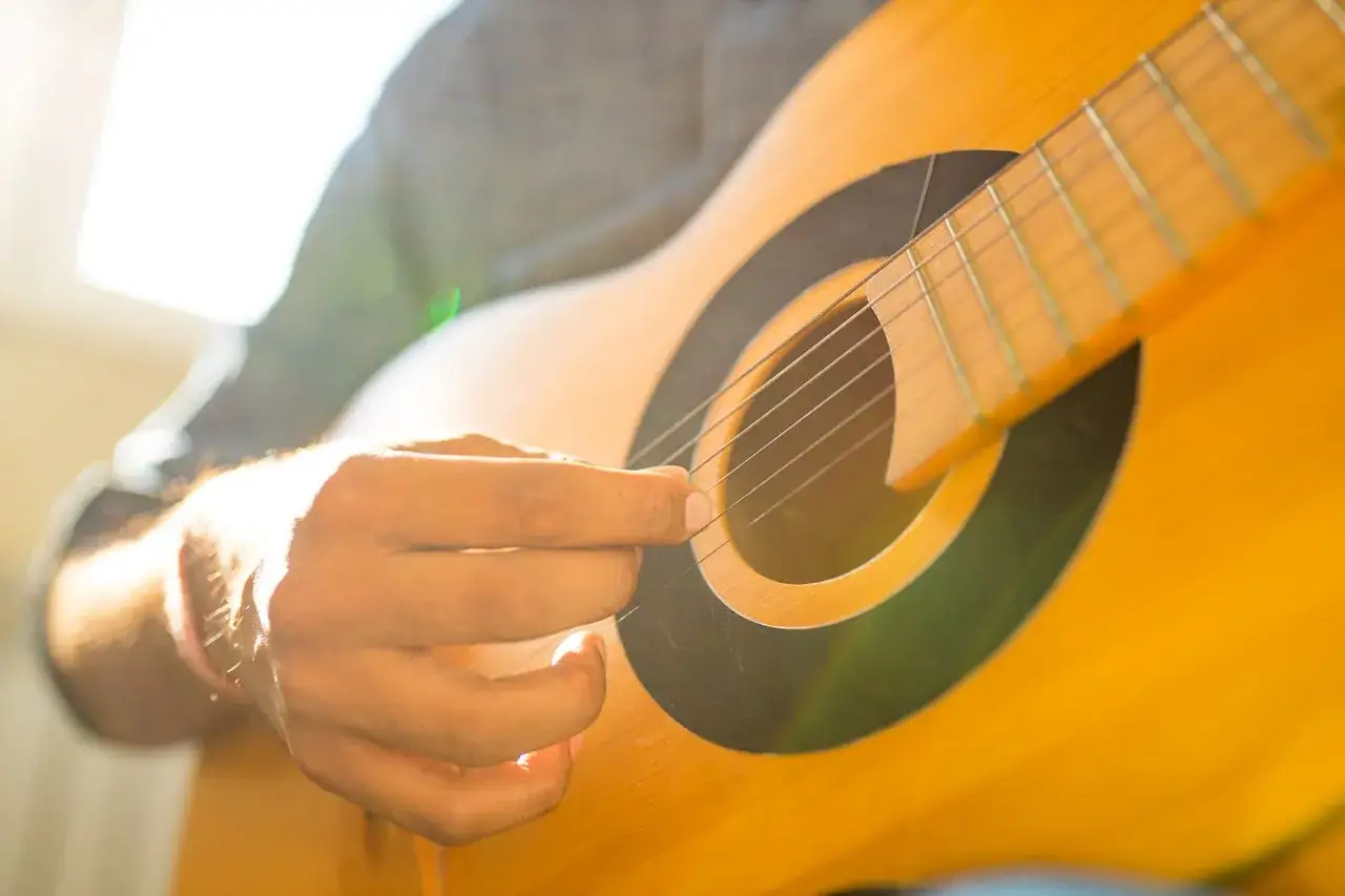 Eine Hand zupft die Saiten einer Gitarre im warmen Sonnenlicht.