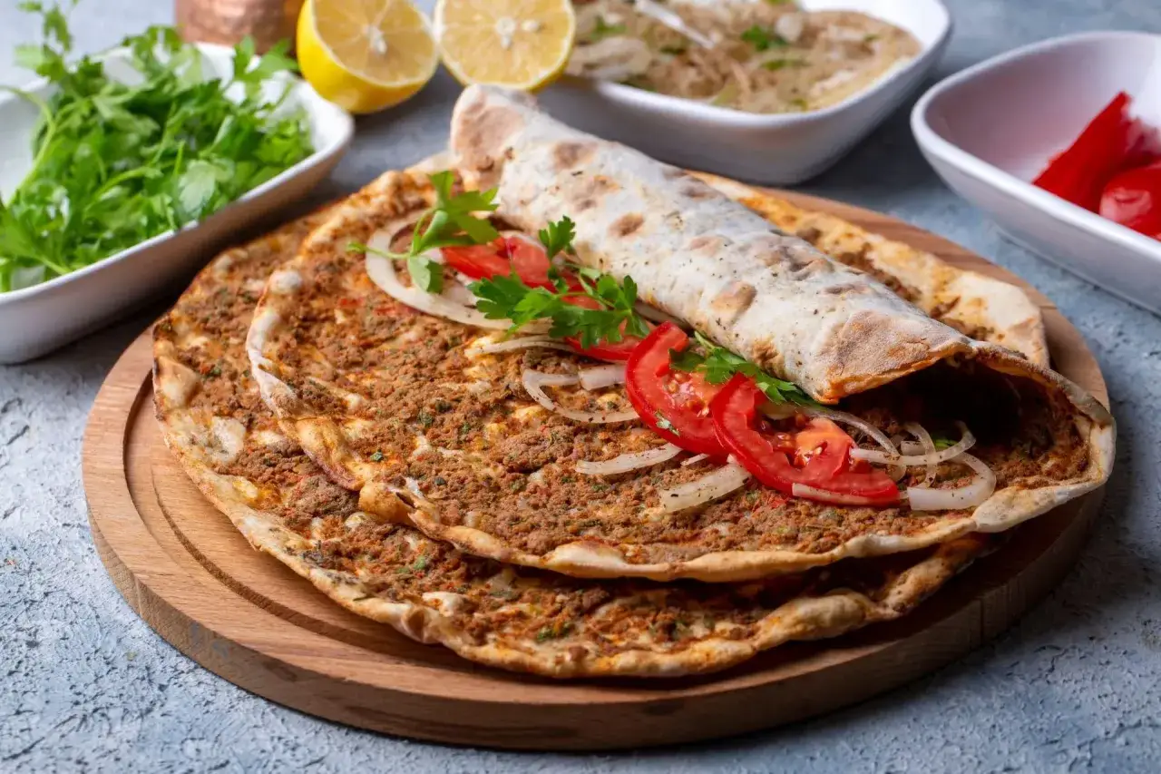 Lahmacun przepis: chrupiące placki z mięsem mielonym, pomidorami i cebulą, zwinięte w rolkę. Obok świeża natka, cytryny i pikantne papryczki.