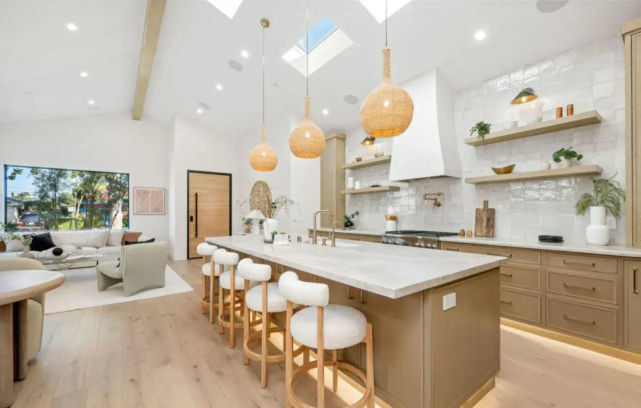Cocinas con isla modernas y luminosas, con isla central de m&aacute;rmol, taburetes blancos y l&aacute;mparas colgantes de mimbre.