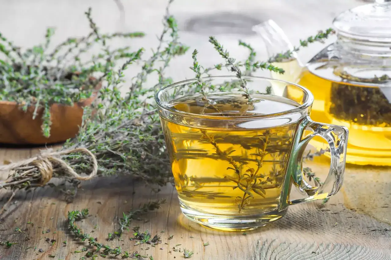 Une tasse de tisane de thym dorée, avec des brins frais et une théière en arrière-plan. Un délice réconfortant.