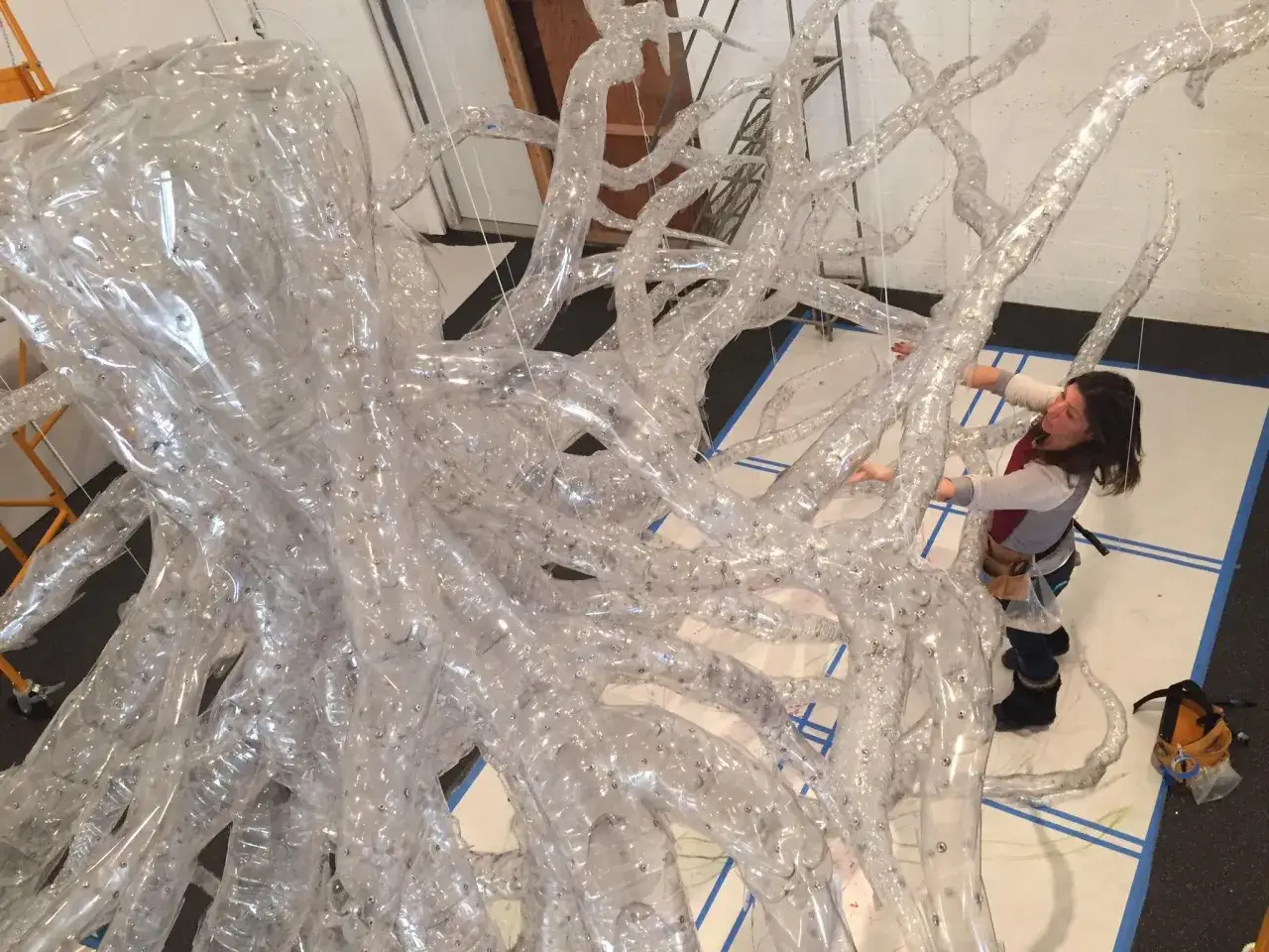Künstlerin arbeitet an einer Installation aus recyceltem Plastik, die wie ein Baum oder ein Korallenriff aussieht. Plastik in der Kunst wird hier neu interpretiert.
