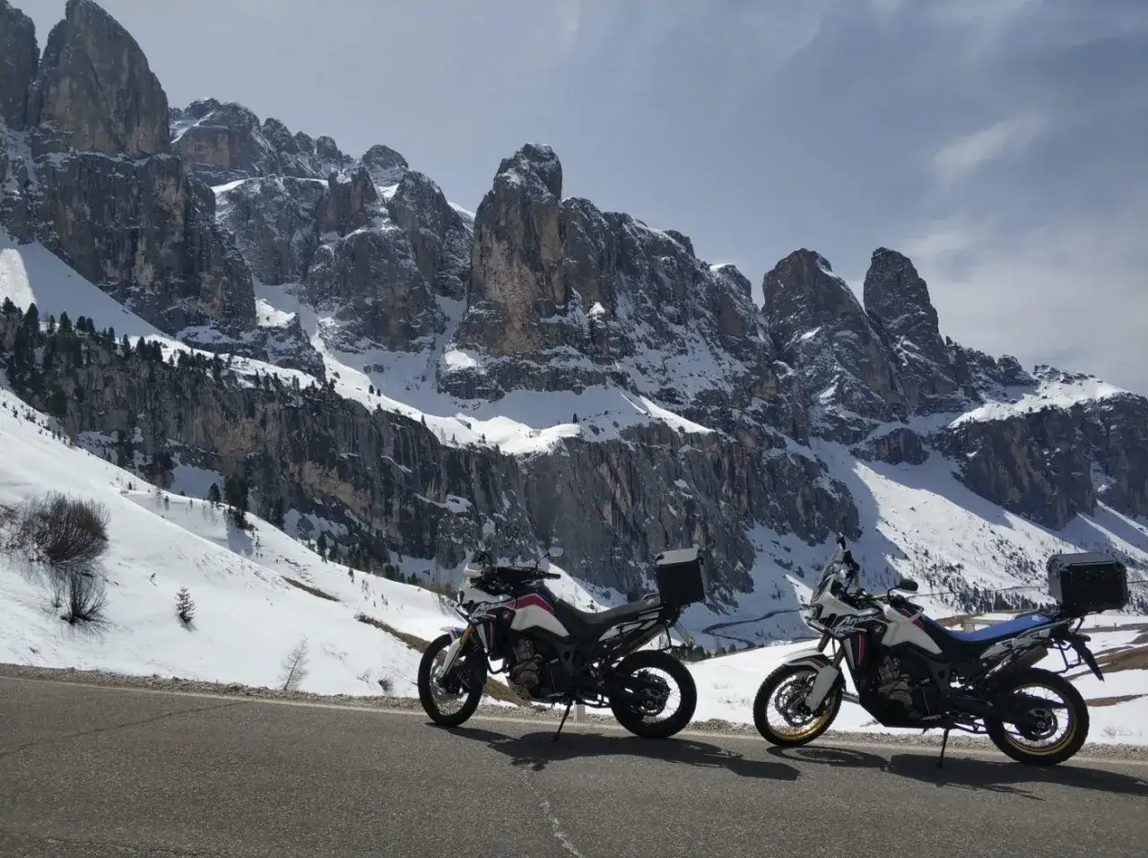 Due moto attendono sul Passo San Lugano, con le imponenti vette innevate a fare da sfondo.