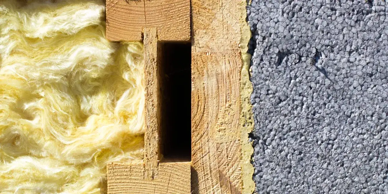 Warstwa izolacyjna z żółtej wełny mineralnej obok drewnianej konstrukcji i szarego styropianu.