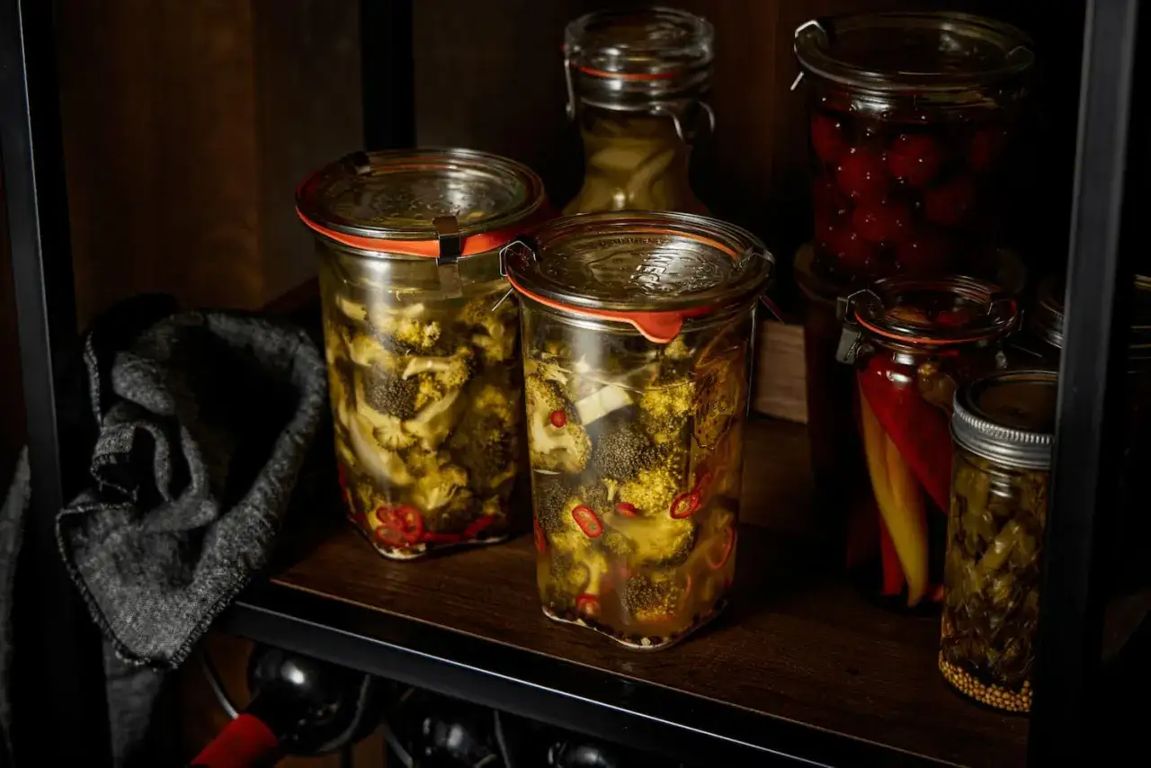 Zwei Gl&auml;ser mit **brokkoli fermentieren**, daneben eingelegte Chilis und Kirschen.
